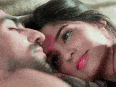 a man and a woman are laying on a bed and the woman is looking at the camera .