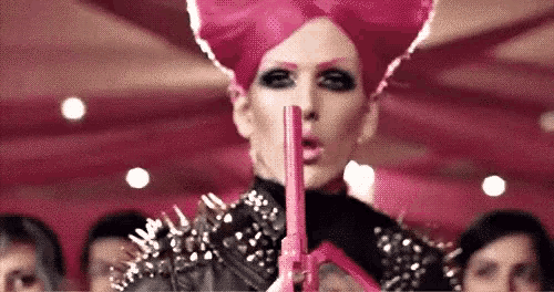 a woman in a pink wig is holding a pink gun in front of a crowd of people .