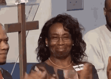 a woman wearing glasses is sitting in front of a cross and making a funny face .