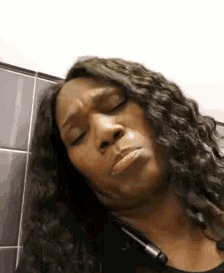 a woman with long curly hair is making a funny face while sitting in a public restroom .