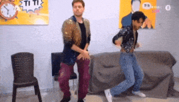 two men are dancing in a room with a clock in the background .