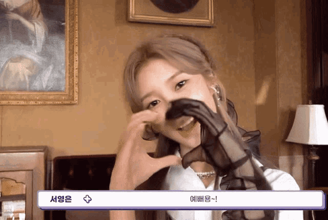 a woman making a heart shape with her hands in front of a painting with korean writing on it