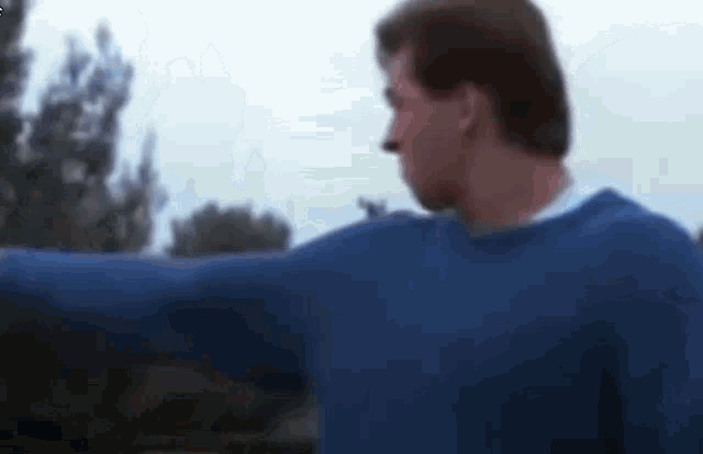 a man in a blue sweater is standing with his arms outstretched in a blurry photo .