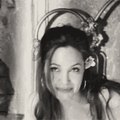 a black and white photo of a woman with a flower in her hair and earrings .
