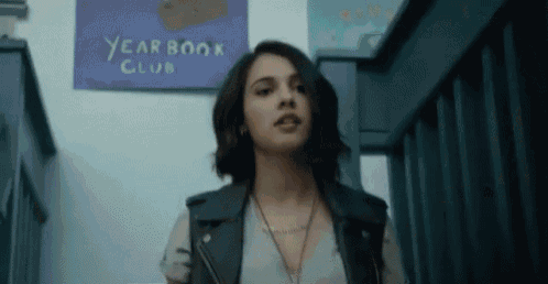 a woman in a leather vest is standing in front of a yearbook club sign .