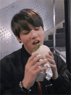 a young man is eating a hamburger wrapped in foil .