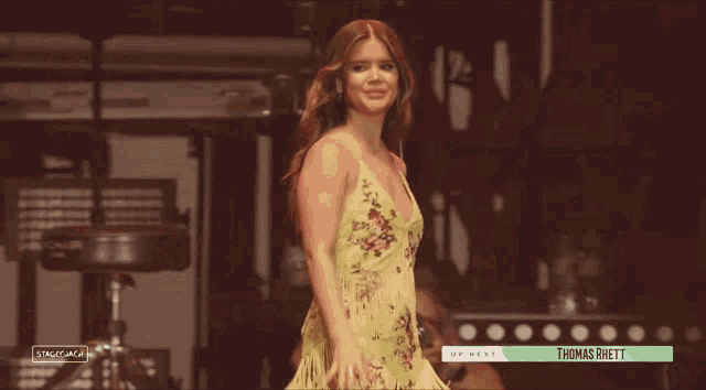 a woman in a yellow dress is waving in front of a sign that says thomas rittt