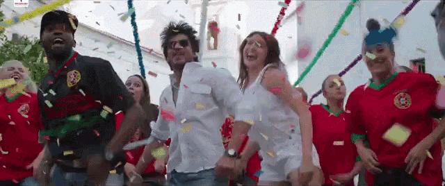 a group of people are dancing in front of a building with confetti falling around them