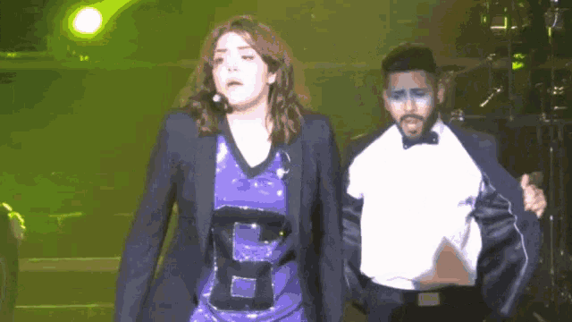 a man in a tuxedo and a woman in a purple shirt with the letter b on it are on a stage