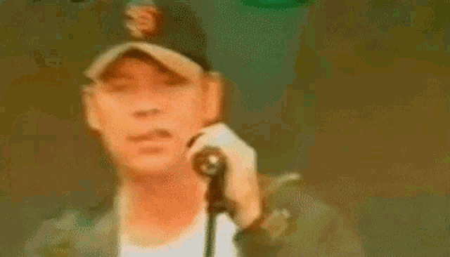 a man in a baseball cap is singing into a microphone while another man watches .