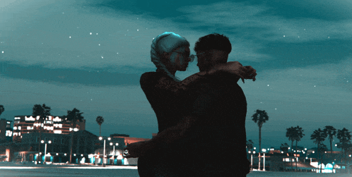 a man and a woman are hugging each other in front of a city at night