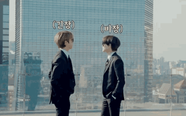 two men in suits and sunglasses are standing next to each other on a balcony with a skyscraper in the background .