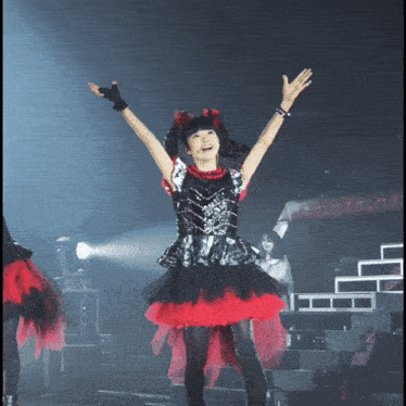 a girl in a black and red dress is standing on a stage with her arms in the air