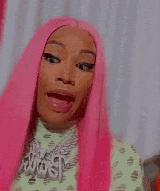 a woman with pink hair is making a funny face while wearing a necklace .