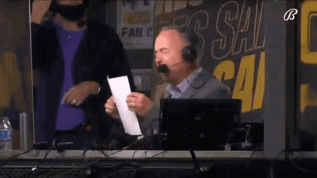 a man wearing a headset stands in front of a sign that says fan