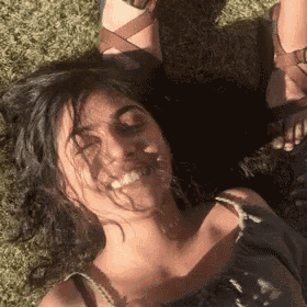 a woman is laying on the grass with her head on her feet and smiling .
