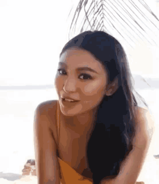 a woman in a yellow bikini is sitting on the beach and smiling at the camera .