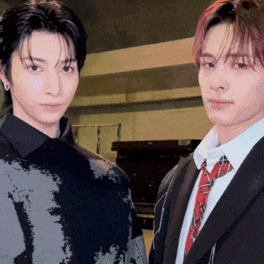 a man in a suit and tie stands next to another man in a black shirt
