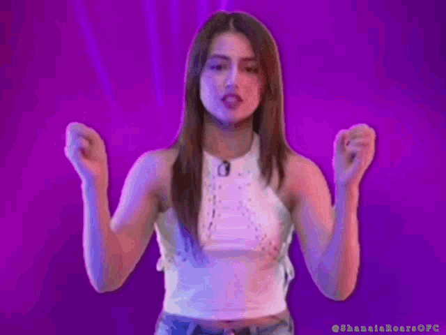 a woman in a white top is making a funny face with her hands in the air .