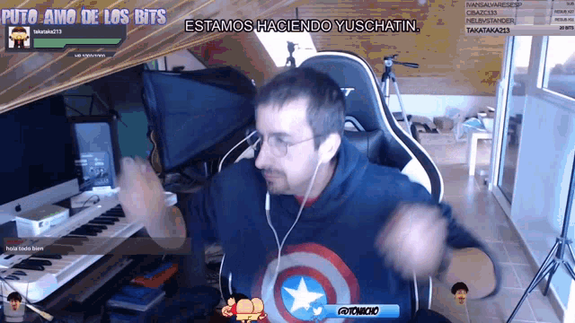a man wearing a captain america sweatshirt is dancing in front of a screen that says " estamos haciendo yuschatin "