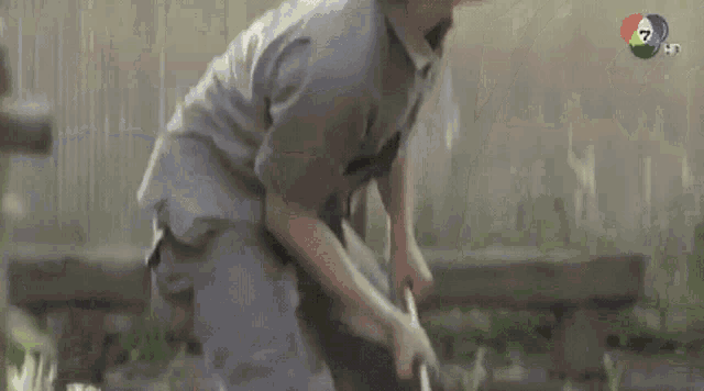 a man in a gray shirt is standing in front of a tree in the rain .