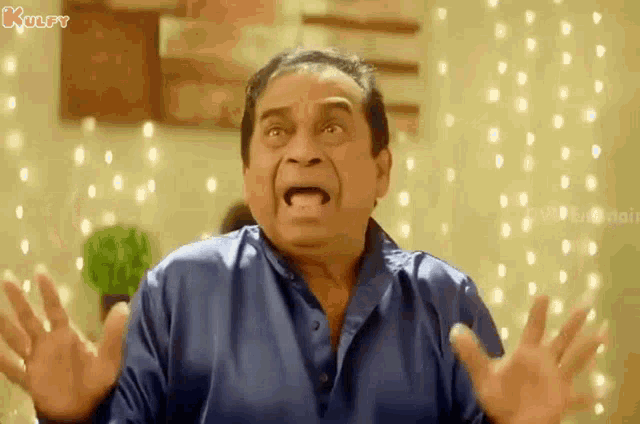 a man in a blue shirt is making a surprised face with his hands outstretched .