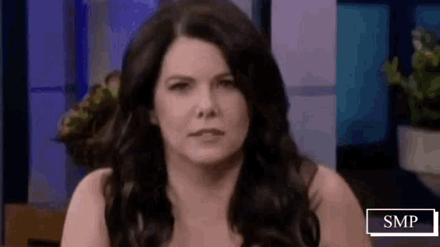 a woman with long black hair is making a funny face while sitting on a stage .