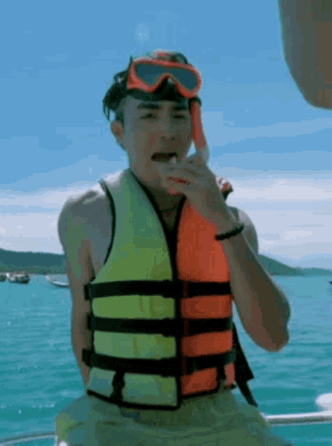 a man wearing a life jacket and goggles is eating a watermelon while sitting on a boat .