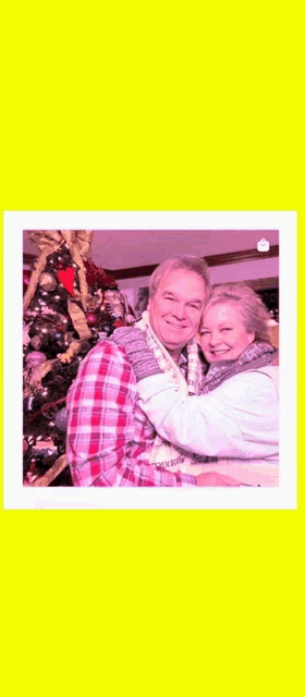 a man and woman hugging in front of a christmas tree .