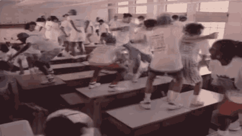 a group of people are dancing in a classroom while sitting at desks .