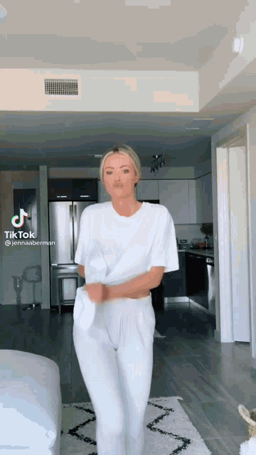 a woman in a white t-shirt and white pants is dancing in a room .