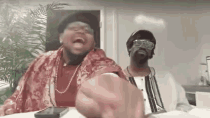 two men are sitting at a table laughing and making a fist .