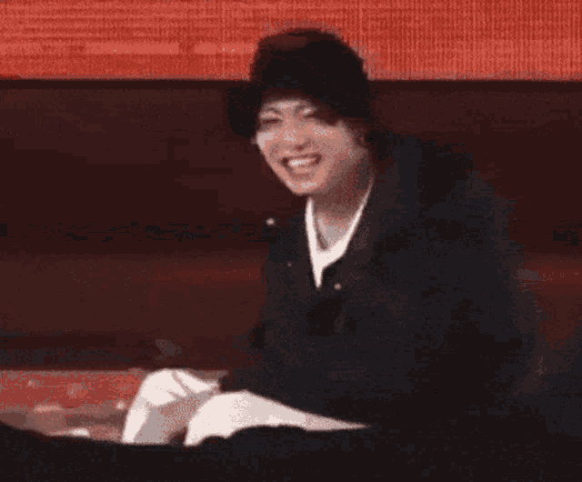 a young man wearing a hat and a jacket is sitting on a stage and smiling .