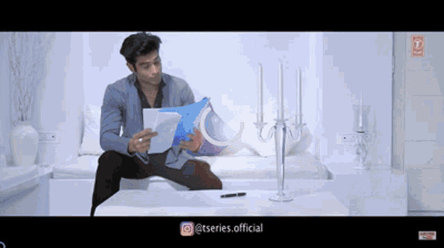 a man sits on a couch reading a book with the hashtag @tseries.official at the bottom of the screen