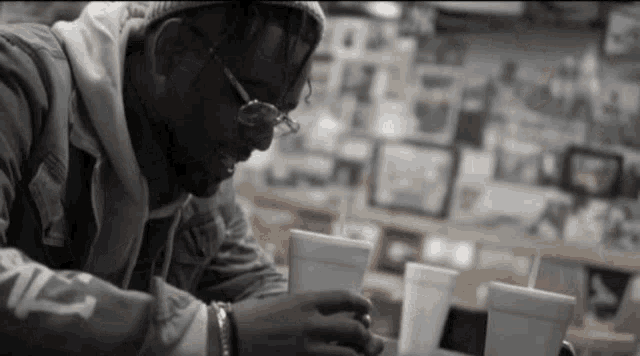 a man wearing glasses sits at a table with two cups of liquid in front of him