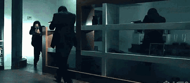 a man in a suit is holding a gun while another man looks on