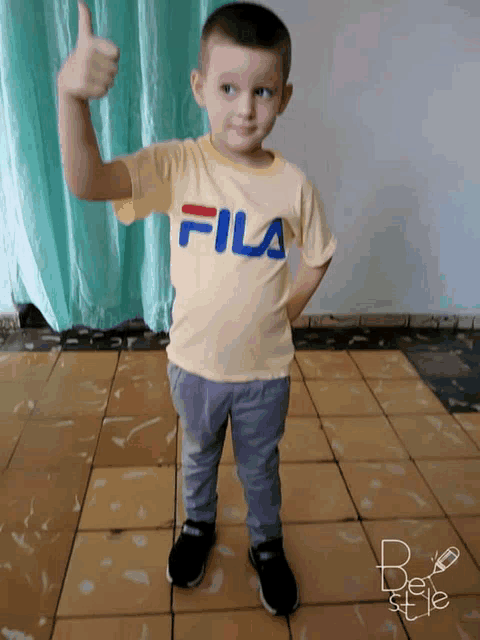 a young boy wearing a yellow fila t-shirt gives a thumbs up