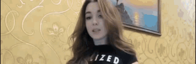 a woman wearing a black shirt with the word ized on it is standing in front of a painting .