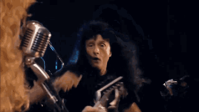 a man with long hair is singing into a microphone