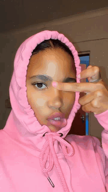 a woman wearing a pink hoodie is giving a peace sign