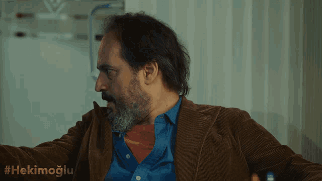 a man with a beard is wearing a blue shirt and a brown jacket with the hashtag #hekimoglu