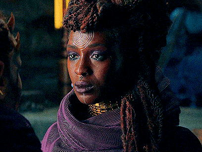 a close up of a woman with dreadlocks wearing a purple scarf and a gold necklace .