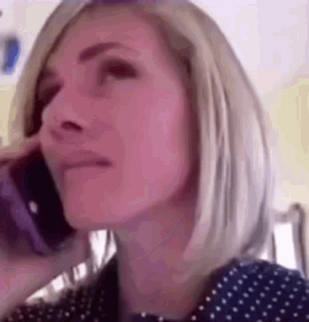 a woman is talking on a cell phone while wearing a blue polka dot shirt .