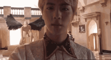 a young man in a white dress with black wings is taking a selfie in front of a statue of an angel .