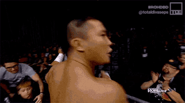 a man without a shirt is standing in front of a crowd at a wrestling match .