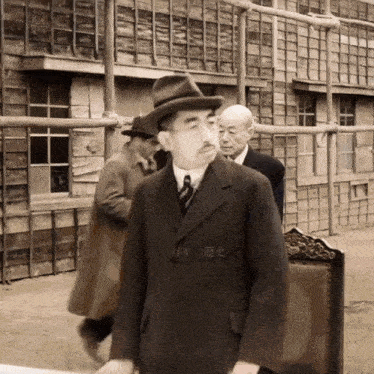 a man in a suit and hat stands in front of a building with chinese writing