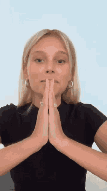 a woman in a black shirt is praying with her hands folded .