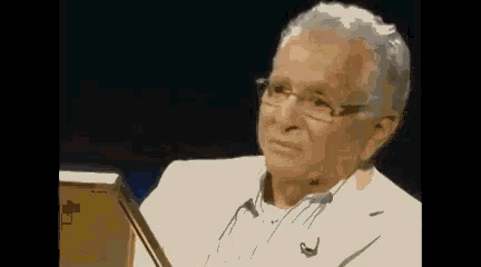 an elderly man wearing glasses and a white jacket is sitting in front of a laptop computer .
