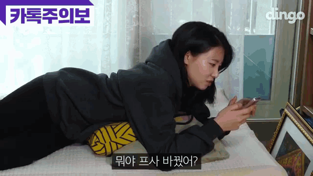 a woman laying on a bed looking at her phone with dingo written on the bottom right