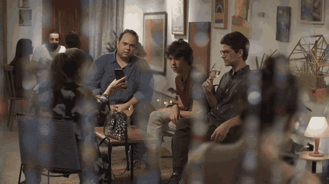 a group of people are gathered in a room and one man is holding a glass of wine